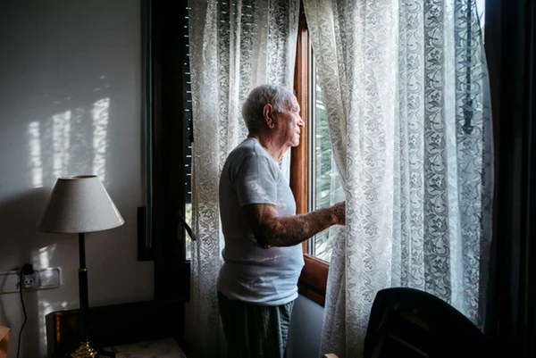 Imagem colorida: idoso observa a rua pela janela - Metrópoles