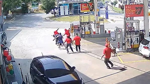 Imagem colorida mostra grupo de frentistas vestidos de vermelho em volta de um homem com capacete vestido de preto; bandido tentou assaltar um posto de gasolina em Cotia e acabou apanhando - Metrópoles