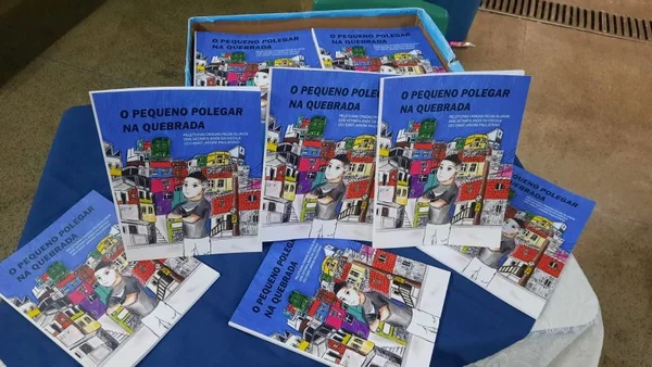 imagem colorida mostra livros espalhados em cima de uma mesa. a capa deles têm o título "O Pequeno Polegar da Quebrada" e uma ilustração com casas e um menino- Metrópoles