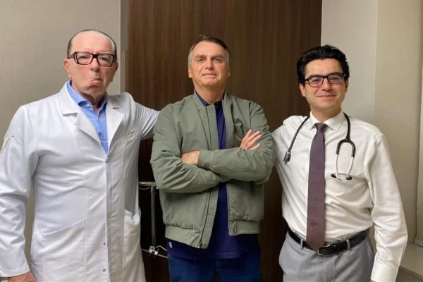Imagem colorida de Jair Bolsonaro, de braços cruzados, entre dois médicos - Metrópoles