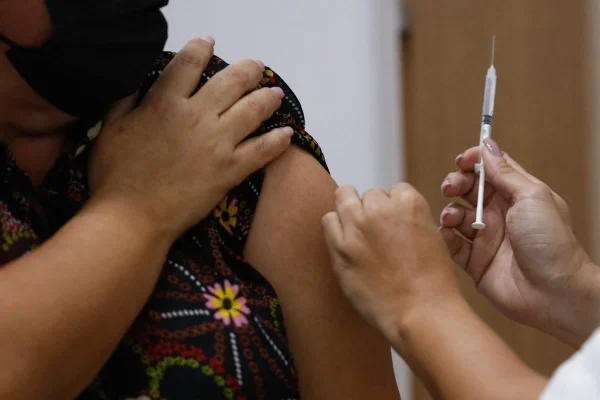 uma mulher segurando a manga da blusa para receber uma dose de vacina