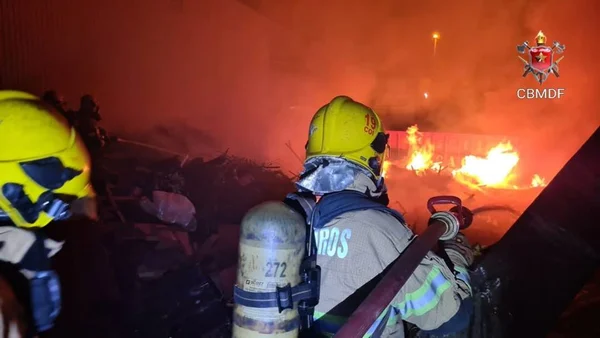 Bombeiro com mangueira no ombro e chamas ao fundo