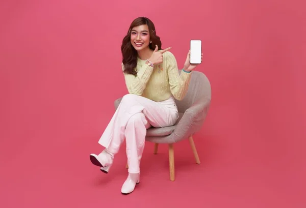 Mulher sentada na cadeira apontando pro celular com sorriso no rosto - Metrópoles