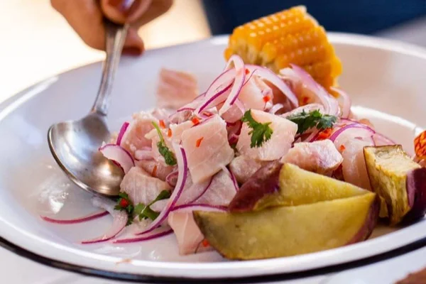 Prato branco com ceviche, peixe, milho e batata-doce