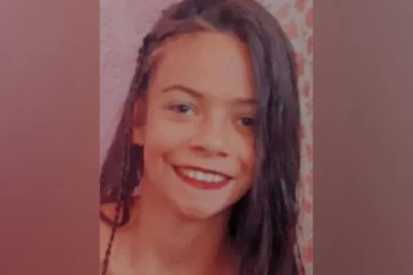 Rosto de adolescente com cabelos escuros sobre parte do lado direito do rosto. Ela tem olhos escuros e sorri.