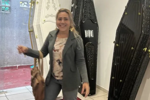 Loira de cabelos soltos sorri, em frente de caixões - Metrópoles