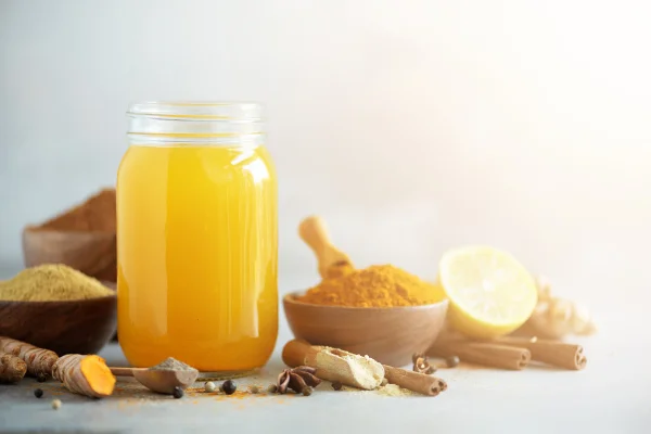Ingredientes para bebida de cúrcuma laranja em fundo de concreto cinza. Água de limão com gengibre, curcuma, pimenta preta. Conceito de bebida quente vegana. Shot de limão e cúrcuma