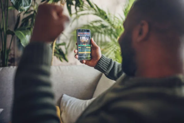 Homem envolvido em apostas esportivas ao vivo no smartphone Um homem adulto em casa, profundamente concentrado no seu smartphone, participa na emoção das apostas desportivas ao vivo, demonstrando intensa concentração