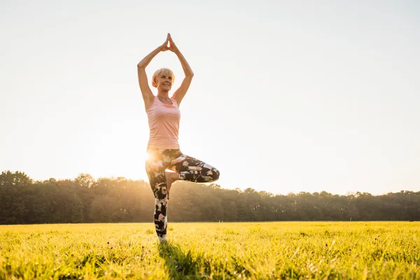 Mulher idosa fazendo ioga em um prado rural ao pôr do sol ou se equilibrando em uma perna só. Metrópoles
