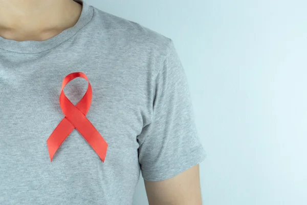 Homem com camisa cinza e broche com símbolo da luta contra o HIV. Hospital - Metrópoles