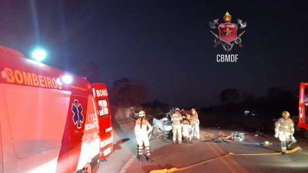 Bombeiros militares andam em via. Vítima no chão e viaturas ao fundo