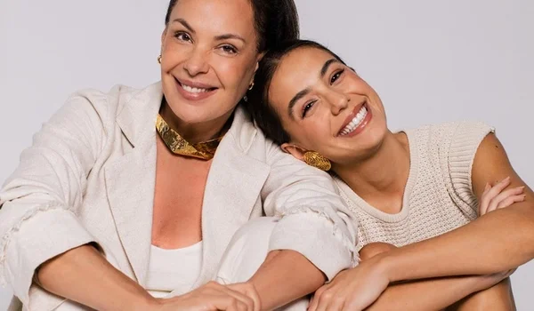 Duas mulheres de roupas brancas e sentadas no chão se apoiando