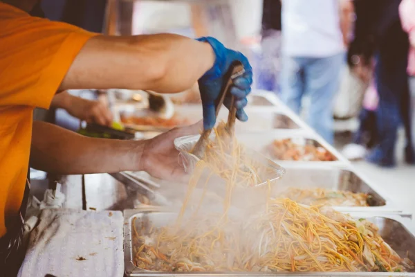 Mão com luva servindo marmita com Yakisoba