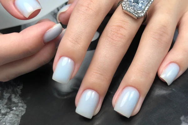 foto colorida mão de mulher com unhas quadradas, brancas e elegante
