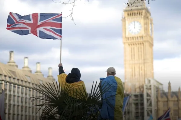 Pessoas de costa seguram uma bandeira do Reino Unido enquanto outro tem uma bandeira da Ucrânia nas costas. Eles olham para o relógio Big Ben, em Londres