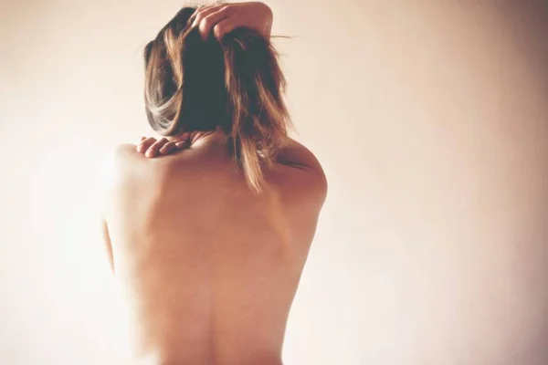 MUlher nua de costas se abraçando em fundo branco - Metrópoles