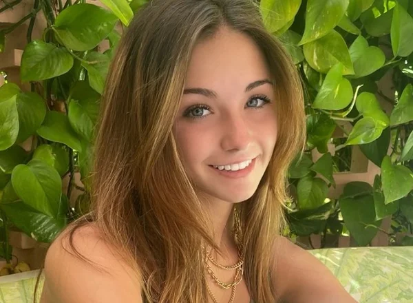 menina branca e de cabelo loiro, olhando para a foto de lado enquanto sorri