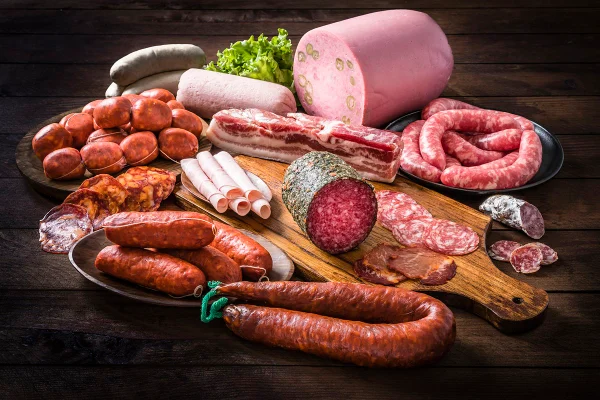 Imagem de vários tipos de salsichas cruas como mortadela, bacon, salame, presunto e salsichas em conserva em um fundo de conceito - Metrópoles