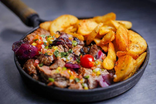 Panelinha com carne, cebola roxa, tomate cereja e batatas assadas