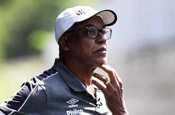 foto colorida mostra Serginho Chulapa usando boné branco do Santos, camiseta escura, óculos e mão no queixo - Metrópoles
