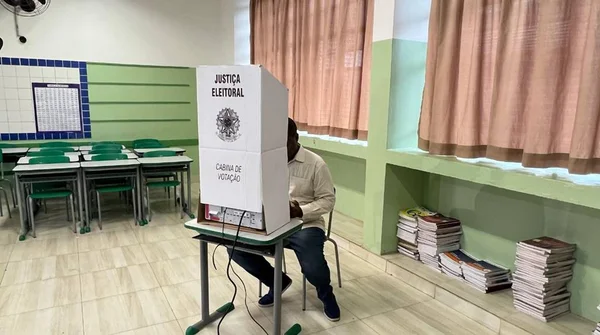 Foto colorida de um homem com camiseta clara e jeans votando - Metrópoles