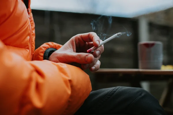 Foto em Close da mão de um homem segurando um cigarro fino e reto - Metrópoles
