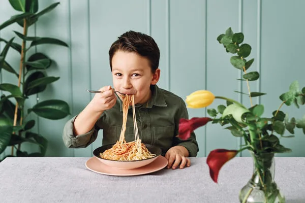 Na foto, uma criança comendo macarrão