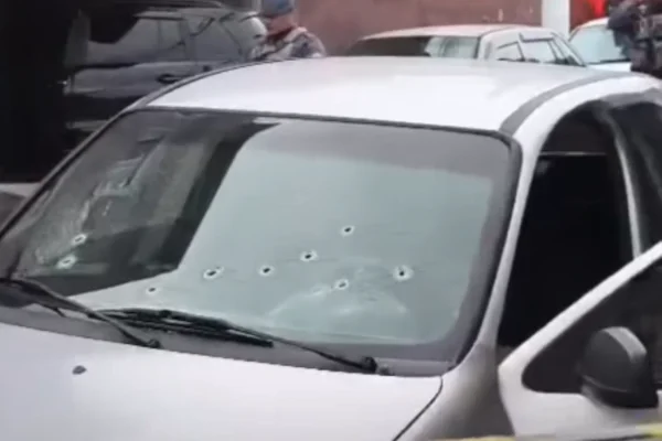 Imagem colorida de marcas de tiros no vidro de um carro cinza. Metrópoles