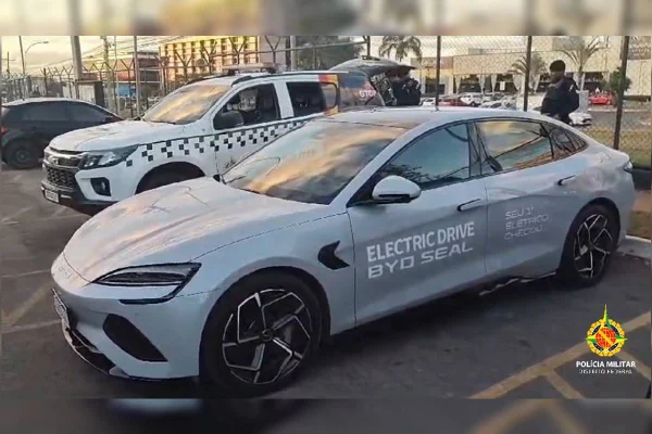 Carro elétrico esportivo em estacionamento de delegacia ao lado de viatura da polícia militar do df
