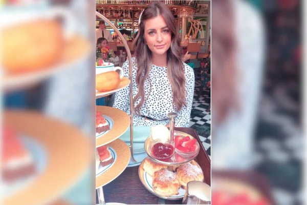Imagem colorida de mulher jovem sentada em uma mesa com vários doces enquanto ela posa para foto - Metrópoles