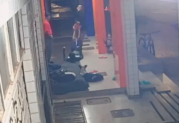 Imagem colorida de um homem em situação de rua sendo arrastado pelas pernas - Metrópoles