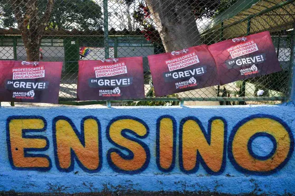 Grade de portão fechada em escola da rede pública. Cartaz de greve dos professores