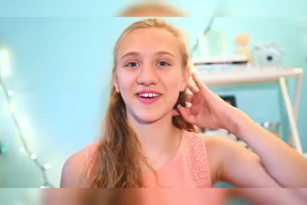 Foto mostra reprodução de vídeo com uma menina loira de cabelos ondulados que ri para a câmera. Ela tem 15 anos, idade em que começou a fumar vape - Metrópoles