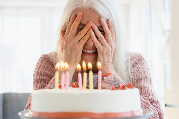 Foto colorida de mulher de cabelos brancos atrás de bolo de aniversário - Metrópoles