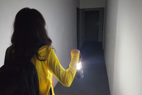 imagem colorida mostra mulher de costas. ela veste uma blusa amarela e segura uma lanterna com a mão