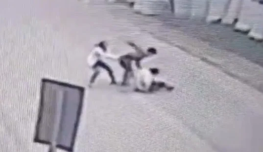 Imagem preta e branca de homem socando outro no meio da rua; ele é contido por uma mulher - Metrópoles