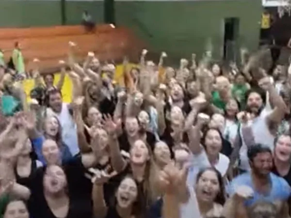 Imagem colorida mostra estudantes cantando hino de faculdade