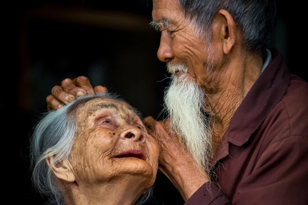Foto colorida de duas pessoas de origem japonesa, idosos, sorrindo um para o outro. - Metrópoles.
