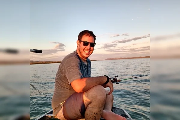 Homem sentado em barco, com óculos escuro, em lago