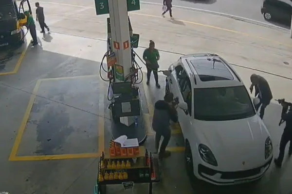 Imagem colorida mostra print de vídeo com ação de três policiais com armas em punho ao redor de carro que está estacionado esperando abastecimento em posto de combustíveis - Metrópoles