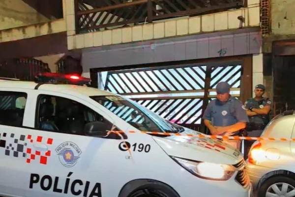 Imagem colorida de viatura da PM na frente da garagem onde homem matou a esposa e se matou na sequência. Metrópoles