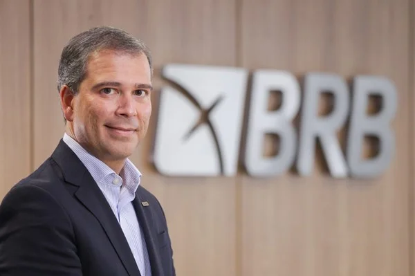 Fotografia colorida de homem de terno com logo do BRB ao fundo em parede