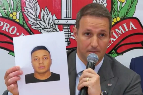 Homem branco, de terno e gravata, fala ao telefone enquanto segura retrato de homem parto - Metrópoles
