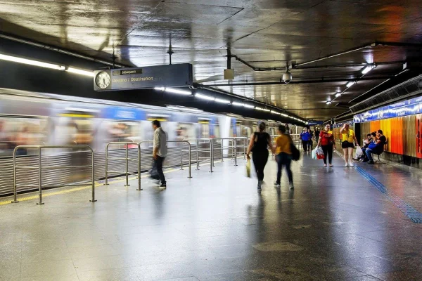Imagens coloridas mostram estação de metrô com pessoas na plataforma e composição se aproximando