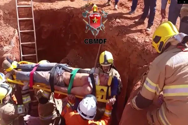 Foto de um um homem sendo carregado em uma maca por bombeiros
