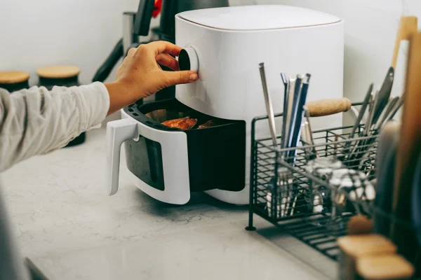 Foto colorida de mão de mulher mexendo em air fryer -Metrópoles