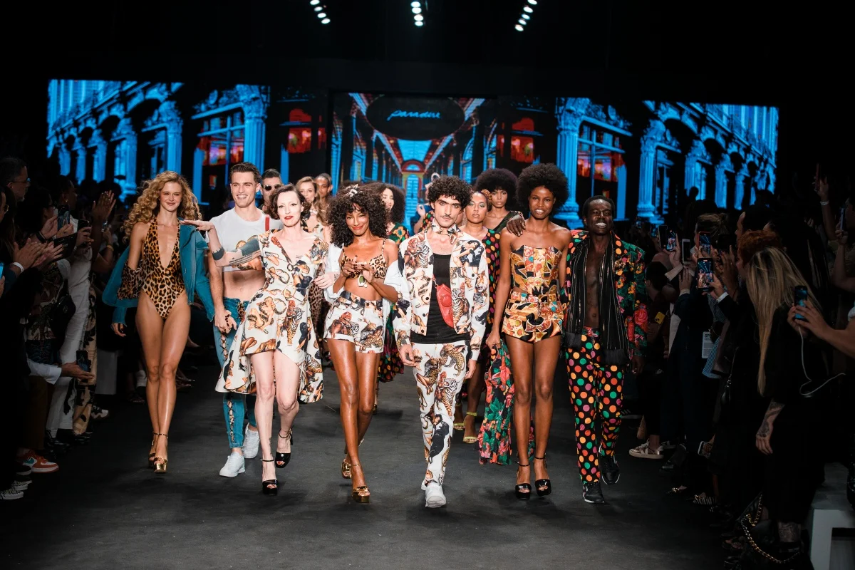 A imagem mostra diversos modelos lado a lado andando em passarela no São Paulo Fashion Week