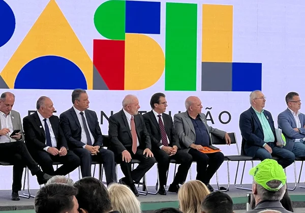 O presidente Lula (ao centro) aparece sentado ao lado do ministro da Previdência, Luiz Marinho em cerimônia com representantes de sindicatos no Palácio do Planalto. Eles aparecem sentados em palco - Metrópoles