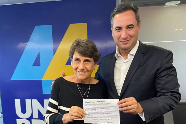 A política Eliana Pedrosa segura sua ficha de filiação ao União Brasil ao lado do presidente da legenda do DF. Ao fundo, um banner com o número da sigla - Metrópoles