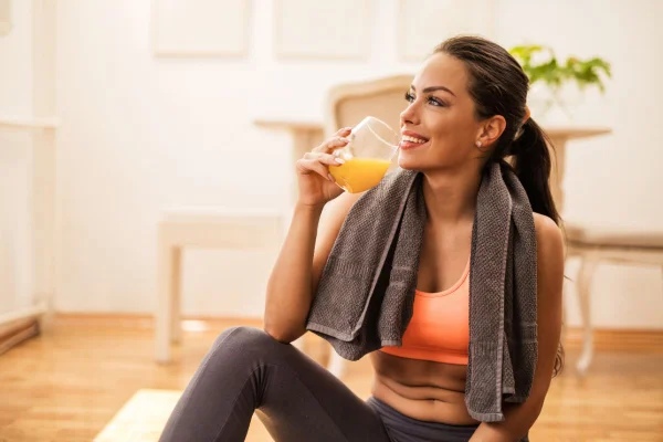 foto colorida de uma mulher bebendo suco após uma atividade física